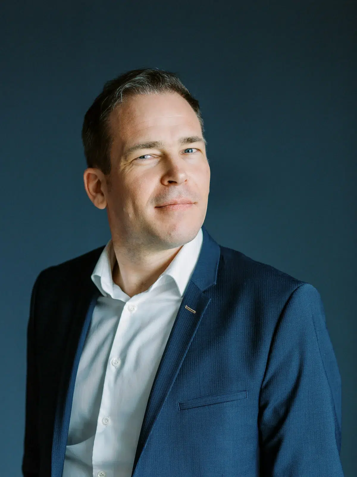 Portrait corporate d'un homme en costume bleu et chemise blanche sur fond sombre.