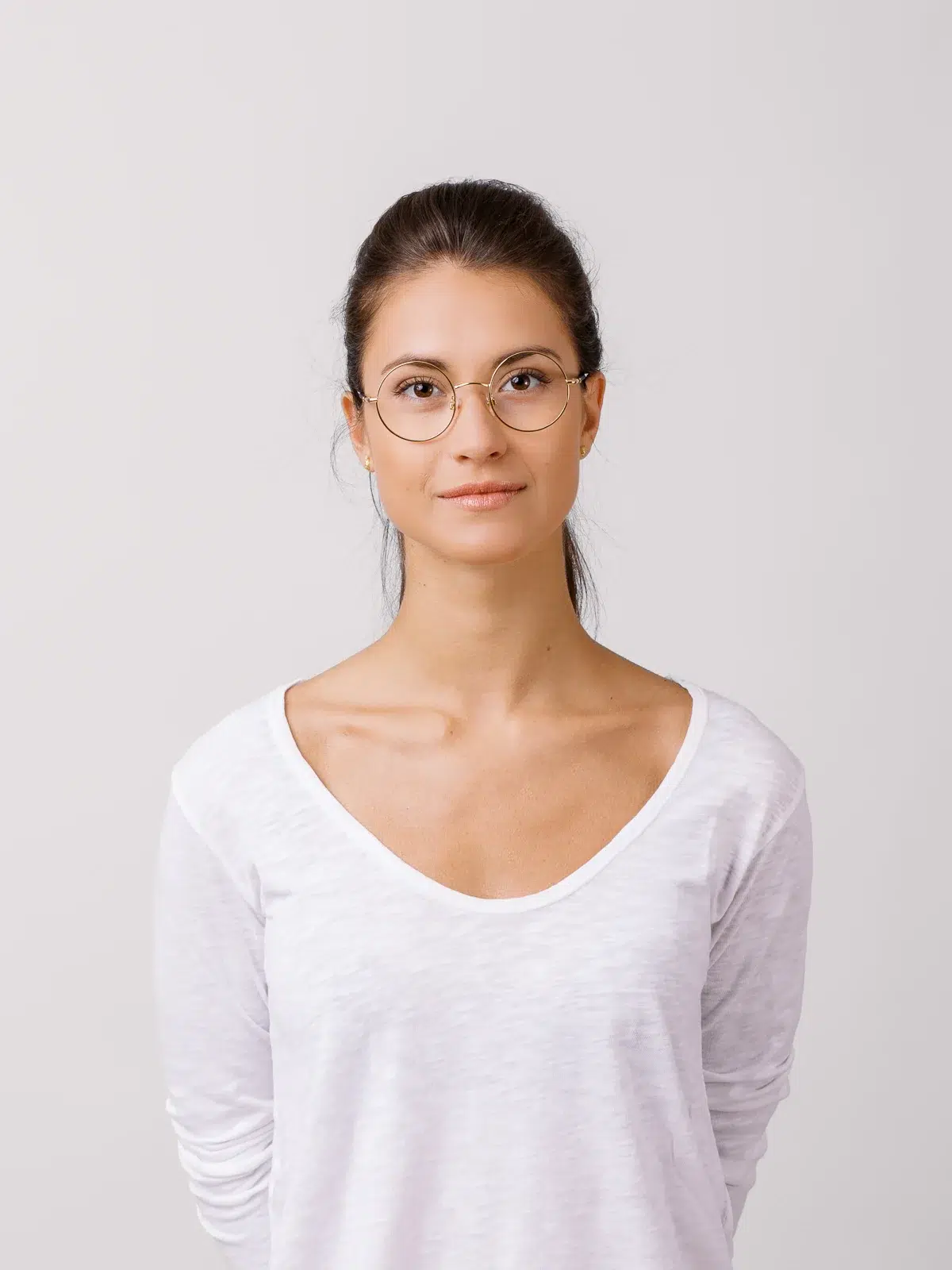 Portrait studio d'une jeune femme portant des lunettes rondes et un t-shirt blanc.