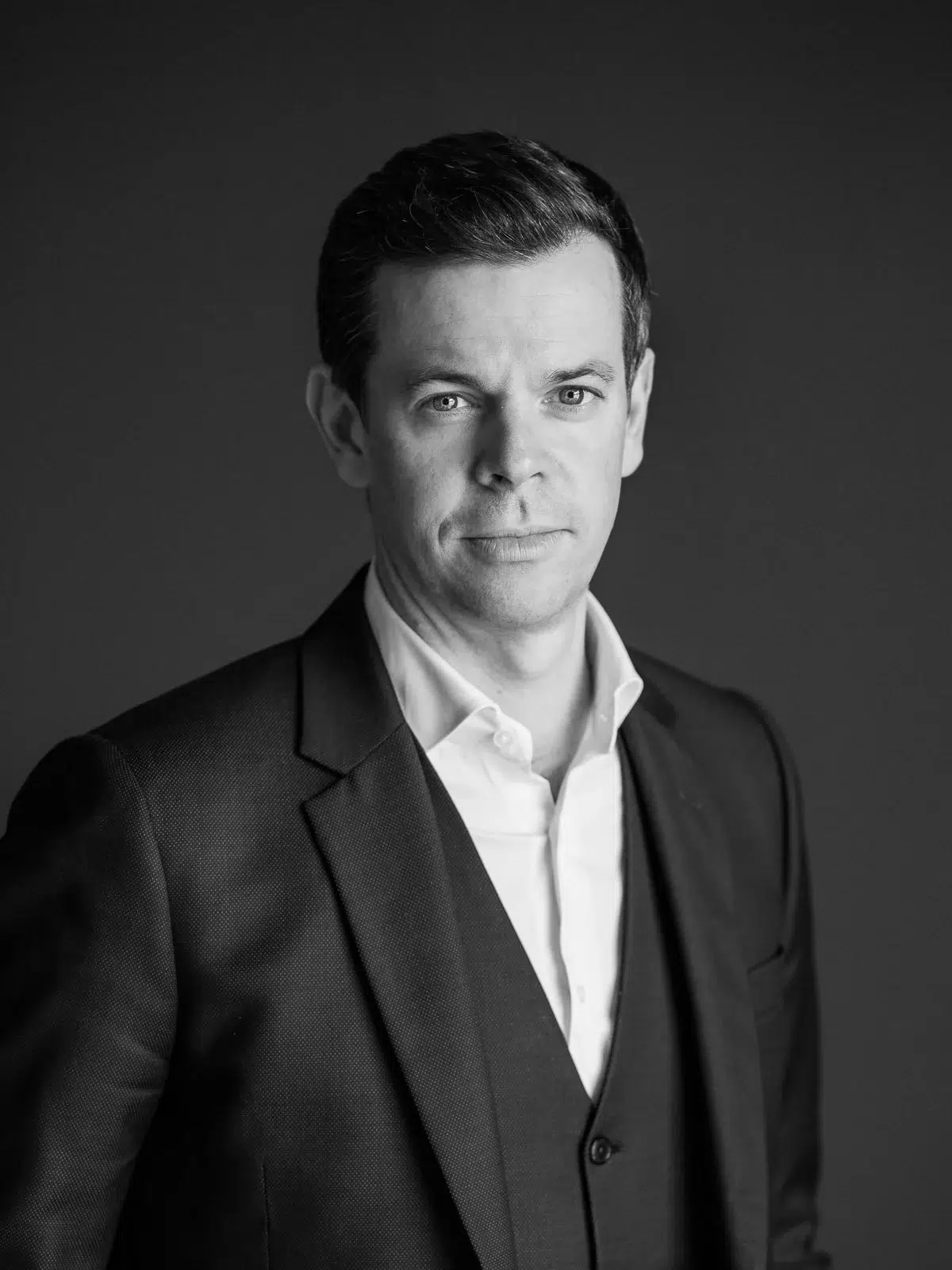 Portrait en noir et blanc d'un homme en costume trois pièces sur fond sombre.