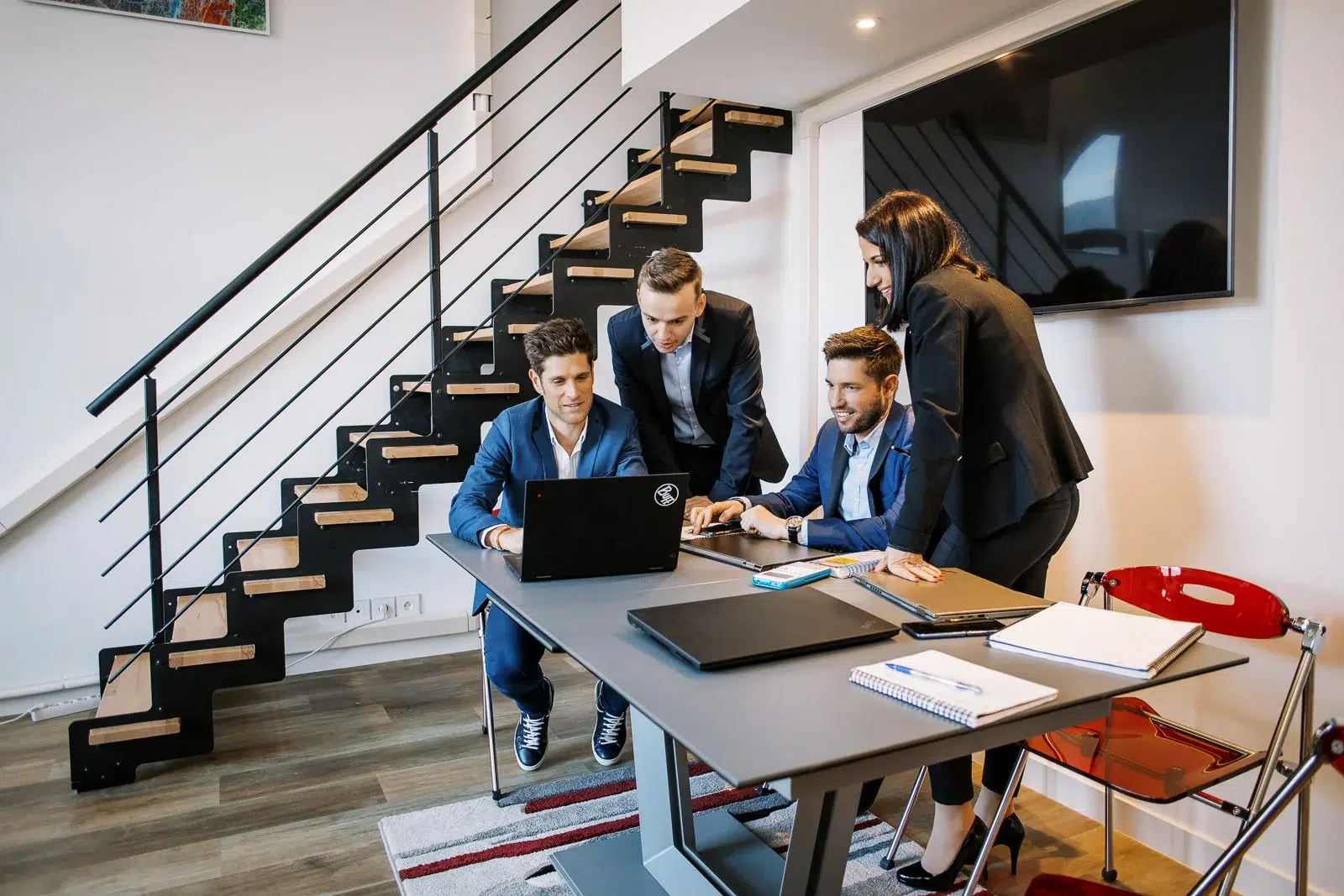 Quatre collègues souriants réunis autour d'un ordinateur portable dans un espace de travail moderne. Photo réalisée par le meilleur photographe corporate Lyon.