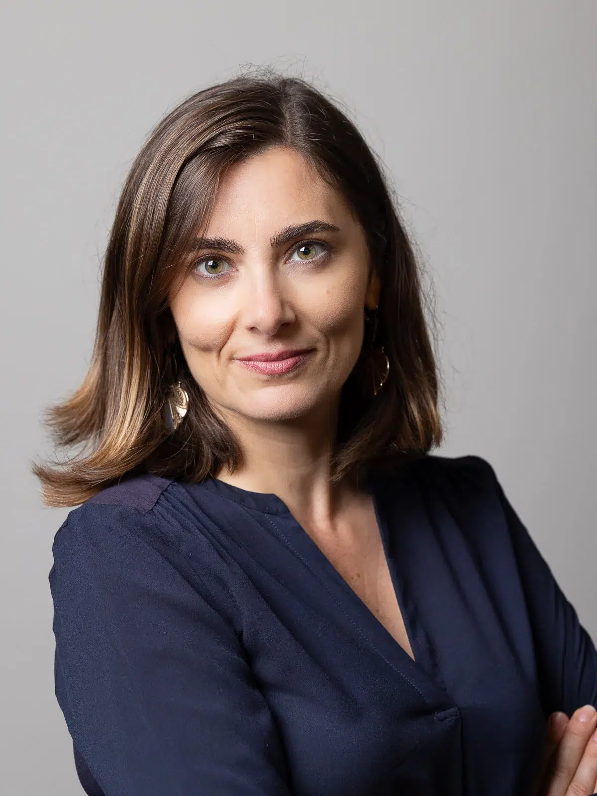 Portrait professionnel d'une femme souriante en chemise bleue sur fond gris.