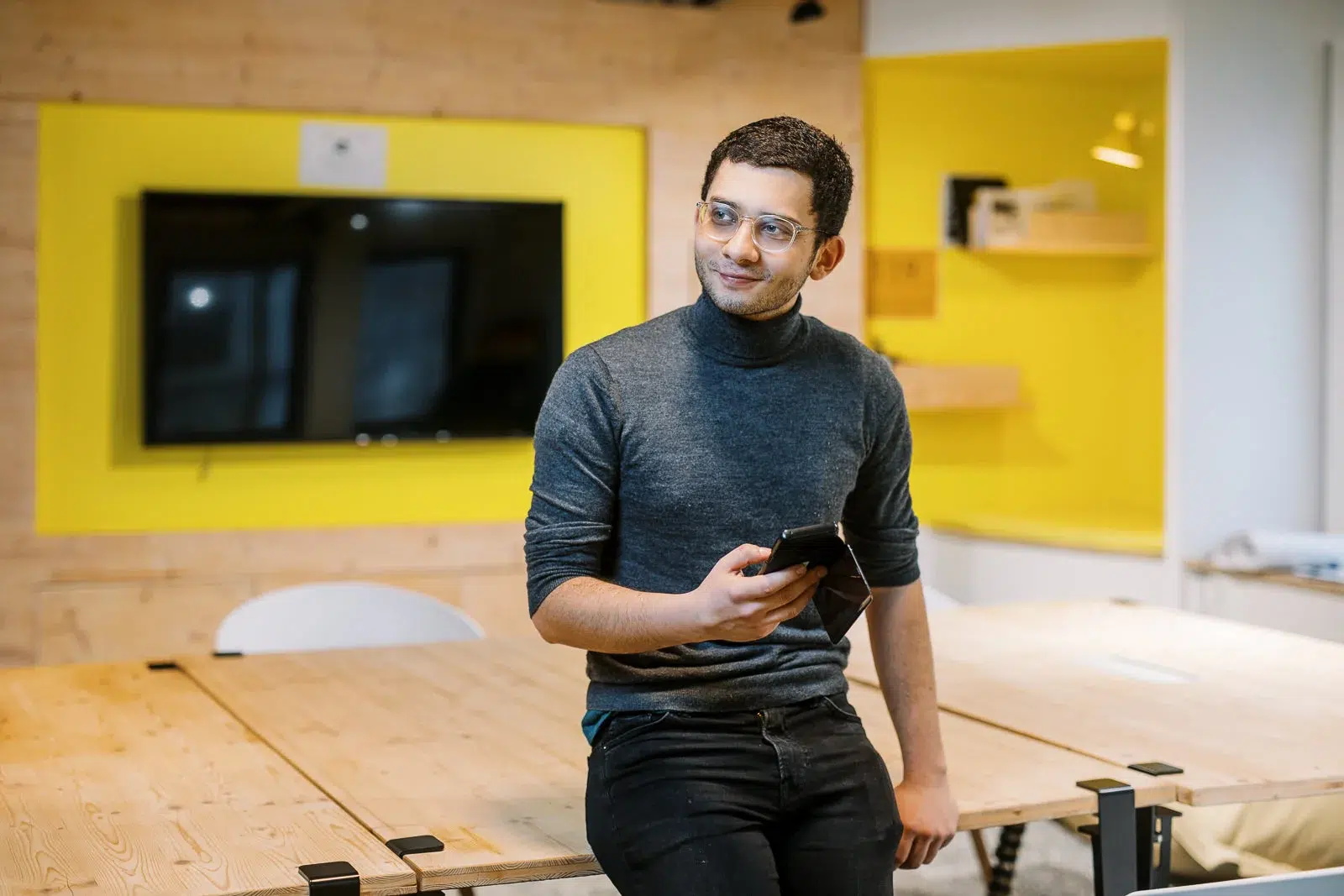 Jeune homme souriant tenant un smartphone dans un espace de travail moderne aux touches jaunes photographié par un photographe corporate Lyon.