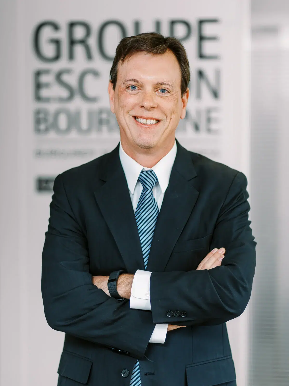 Portrait corporate d'un homme souriant en costume sombre et cravate rayée bleue.