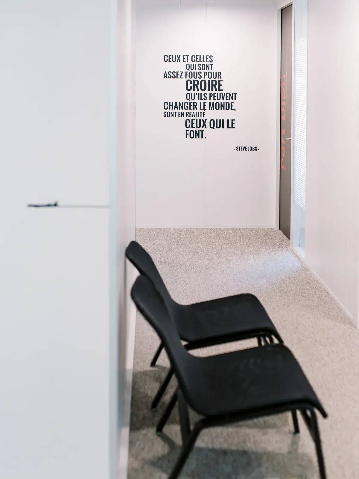 Mur blanc de bureau avec une citation de Steve Jobs en lettres noires et deux chaises noires.