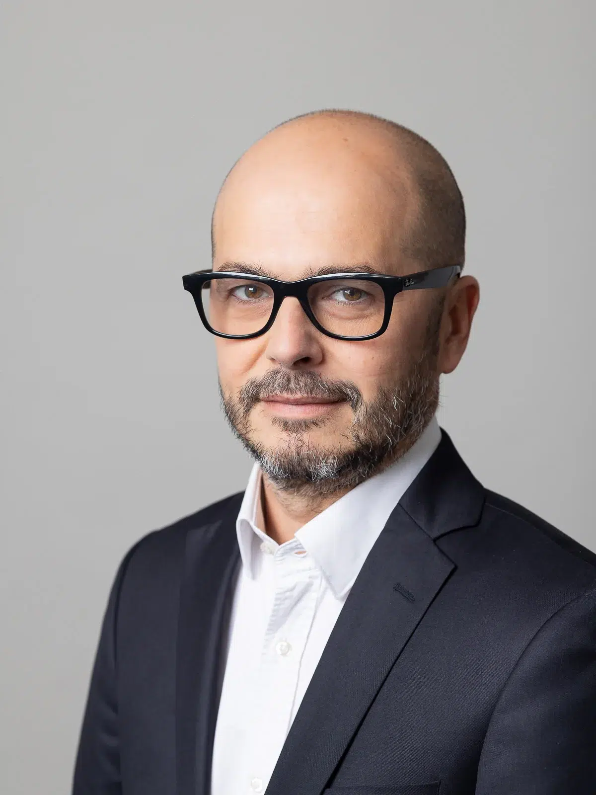 Portrait corporate d'un homme portant des lunettes à monture noire épaisse et un costume sombre.