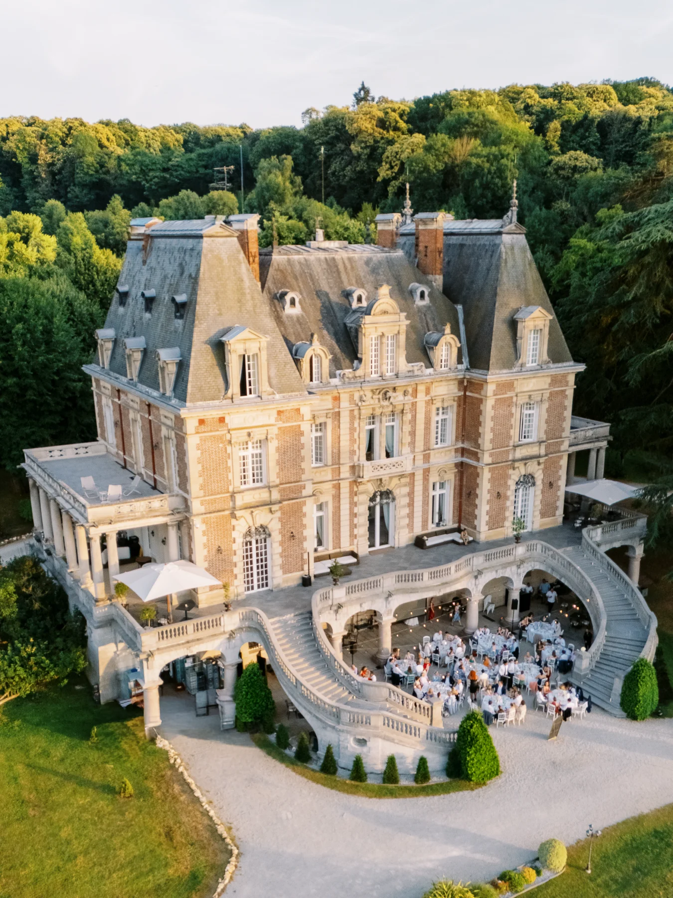 Photographe-evenement-lyon : vue aérienne d'une réception élégante au pied d'un château classique à l'heure dorée.