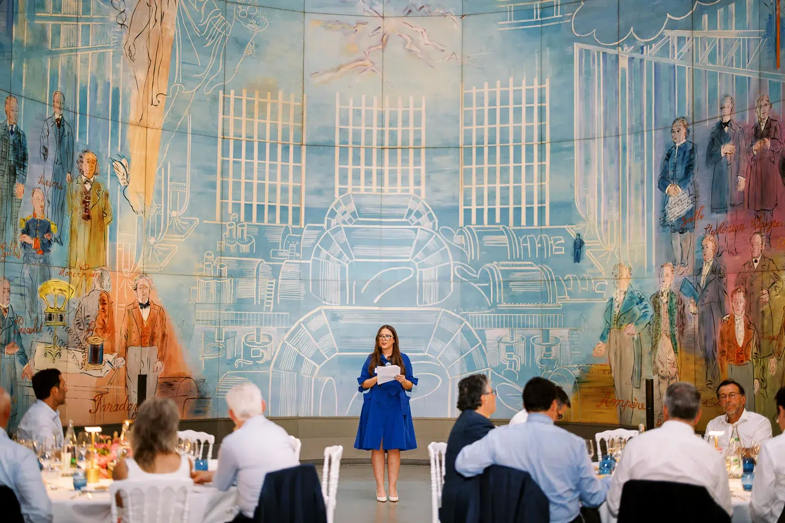 Photographe événementiel Lyon capturant une femme prononçant un discours devant une fresque murale lors d'un dîner.