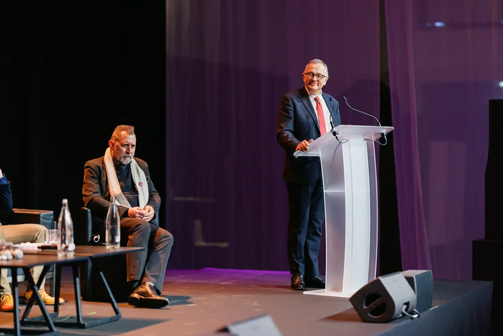 Photographe événementiel Lyon : un homme prononce un discours au pupitre tandis qu'un autre l'écoute attentivement sur scène.