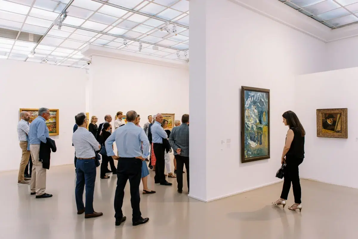 Photographe event Lyon : groupe de personnes observant des tableaux lors d'une visite guidée dans une galerie d'art lumineuse.