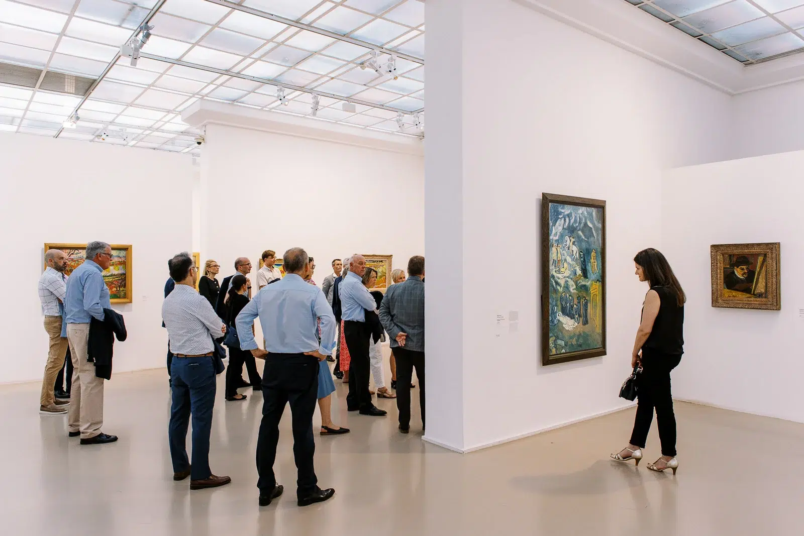 Photographe event Lyon : groupe de personnes observant des tableaux lors d'une visite guidée dans une galerie d'art lumineuse.
