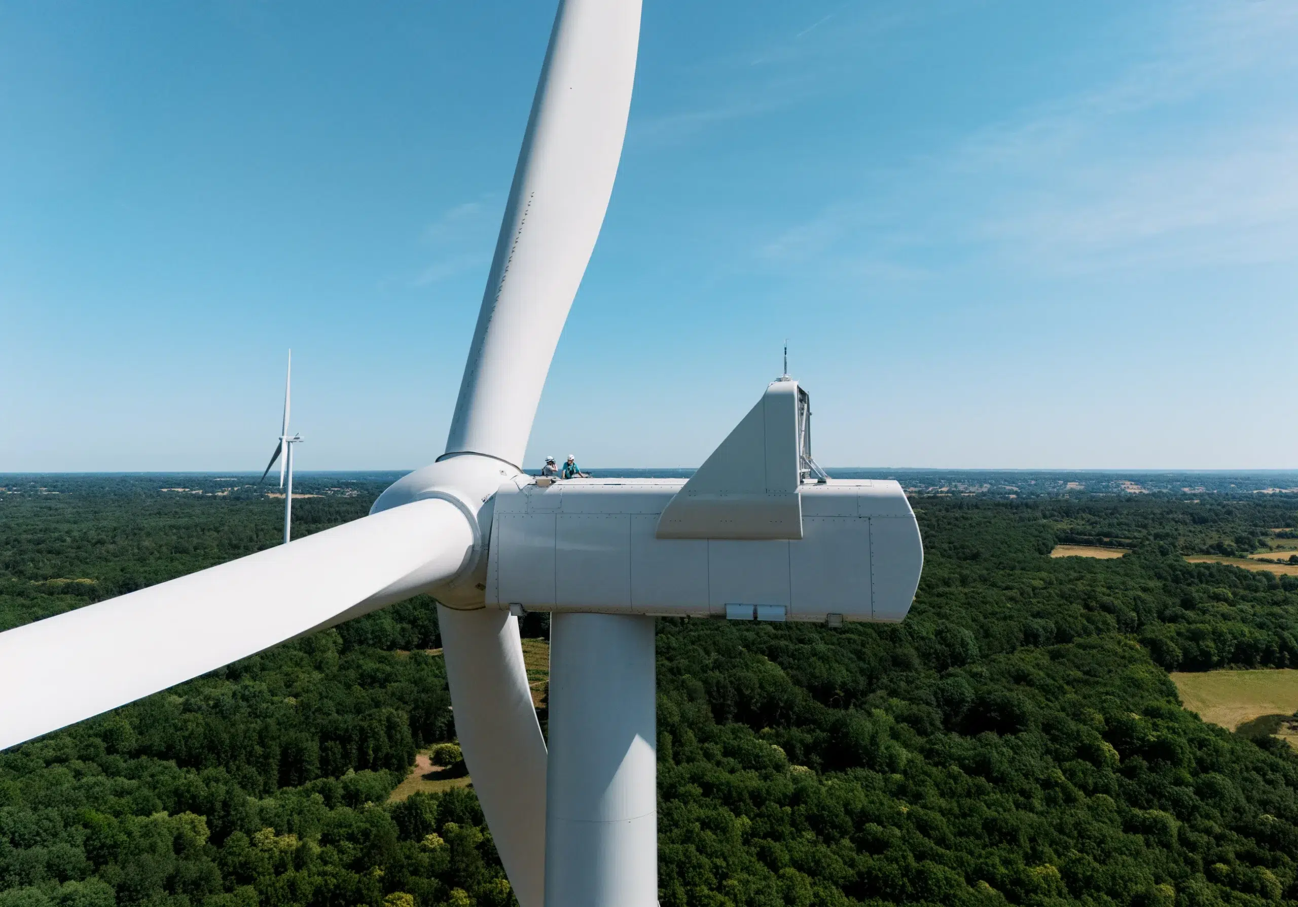 Photographe Lyon éolienne documentant l'inspection d'une nacelle par deux techniciens au-dessus d'une forêt verdoyante.
