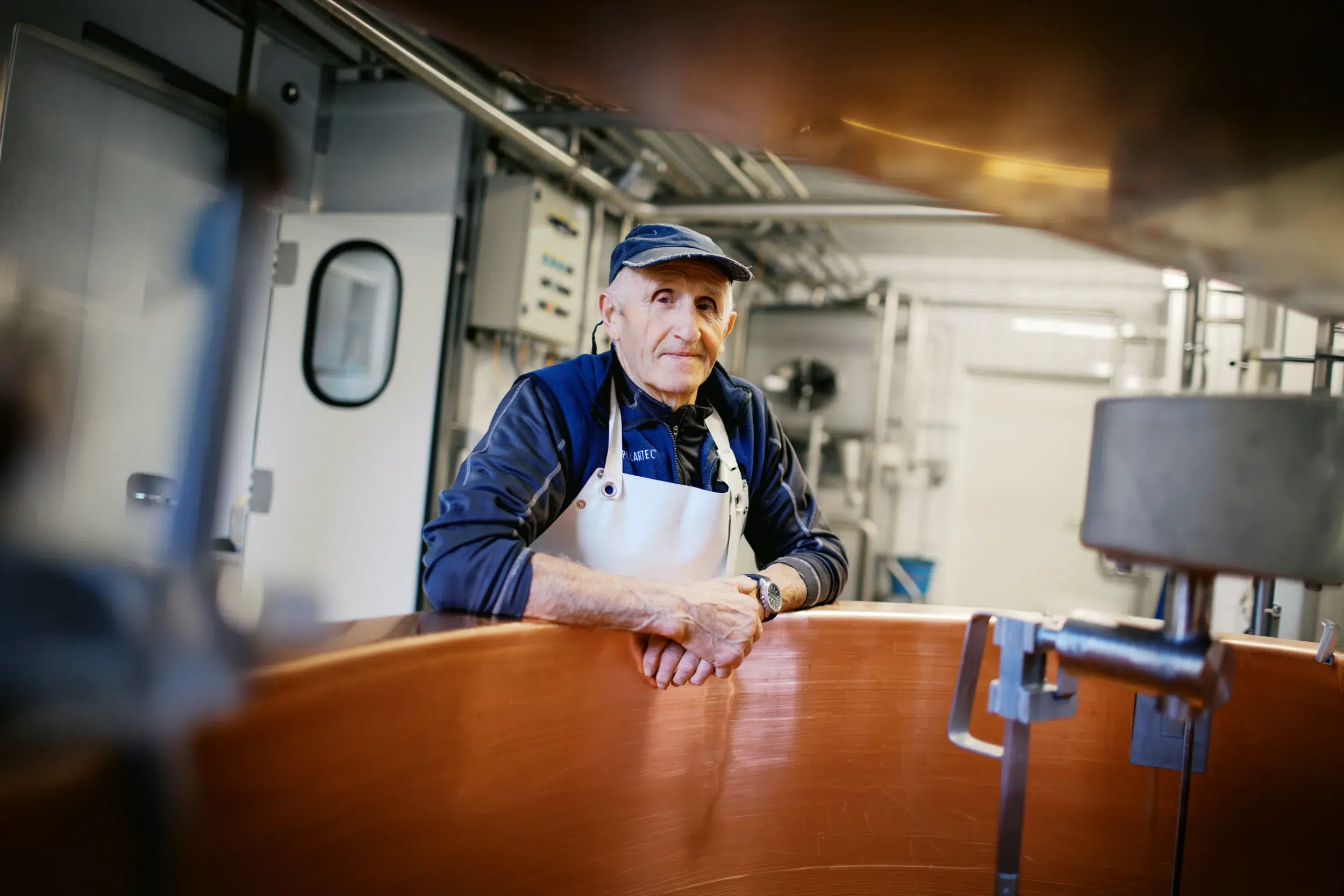 Photographe Lyon : portrait d'un artisan fromager en tablier blanc accoudé à une cuve en cuivre dans son atelier.