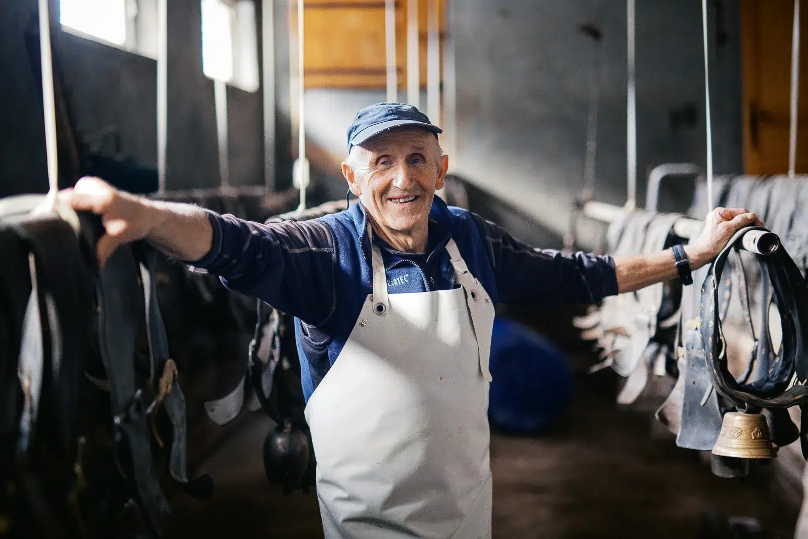 Photographe portrait Lyon : artisan fromager souriant dans son atelier avec cloches de vache.