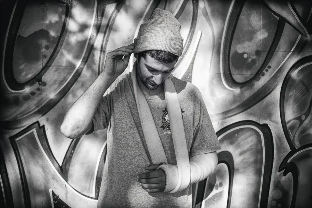 Photographe portrait Lyon : homme avec bras en écharpe devant un mur de graffitis.