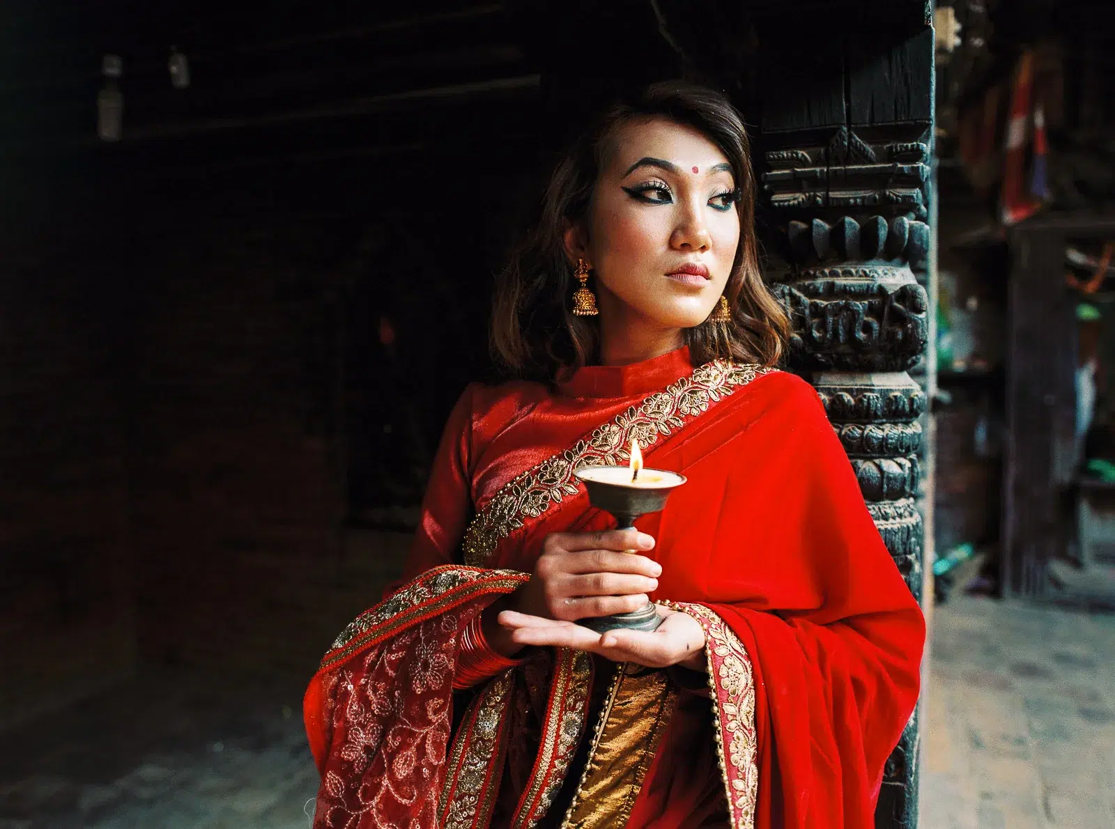 Photographe portrait Lyon : femme en sari rouge tenant une bougie dans un temple ancien.