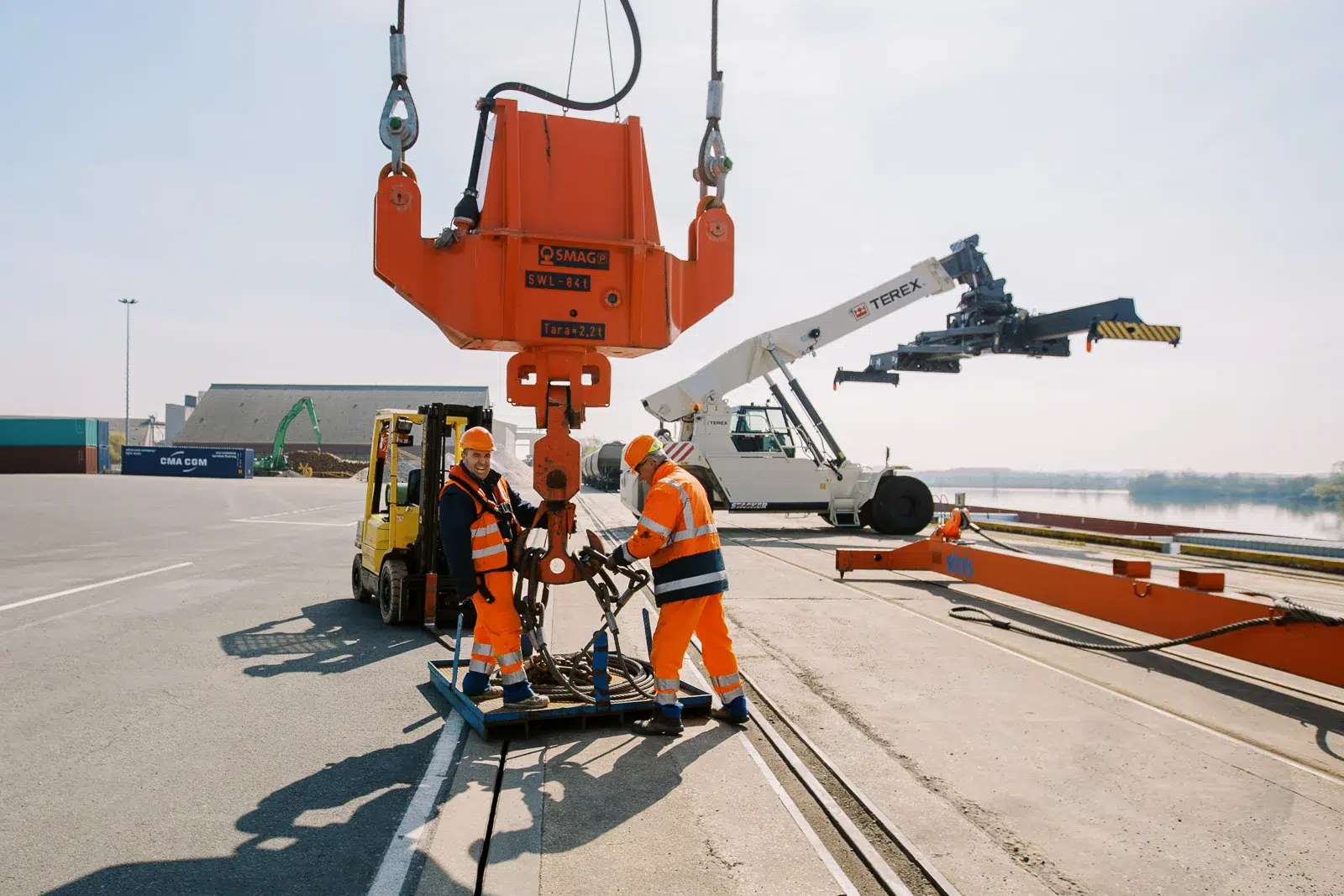 Photographe reportage Lyon : Deux ouvriers attachent des élingues à une grue sur un port.