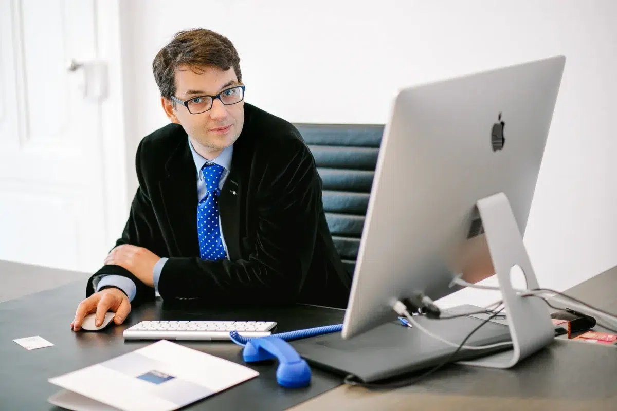 Photographe portrait Lyon : homme à lunettes travaillant sur un ordinateur Apple dans un bureau clair.