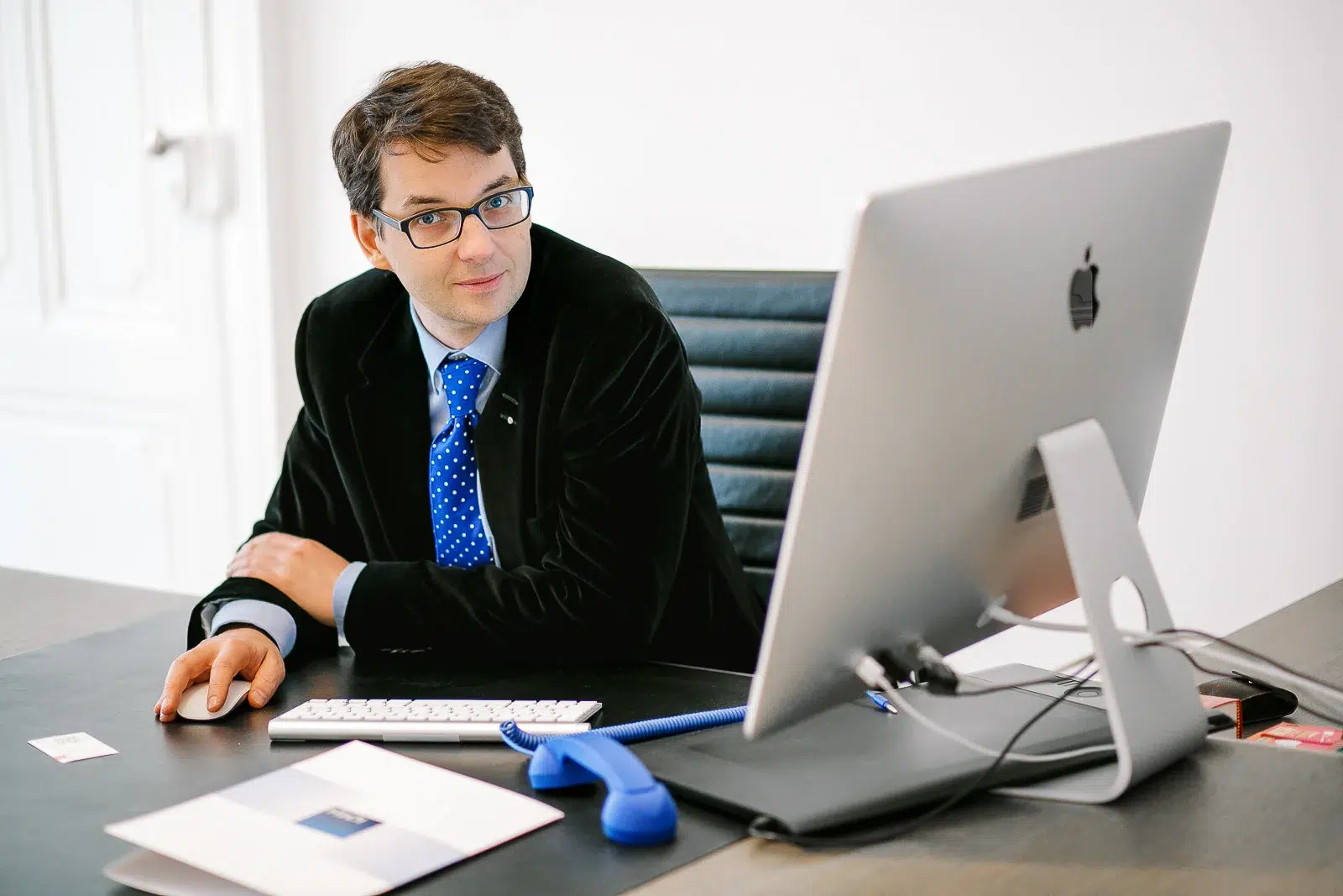 Photographe portrait Lyon : homme à lunettes travaillant sur un ordinateur Apple dans un bureau clair.