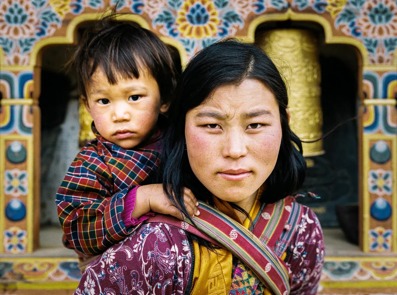 Photographe portrait Lyon : femme bhoutanaise portant son enfant devant un temple coloré.
