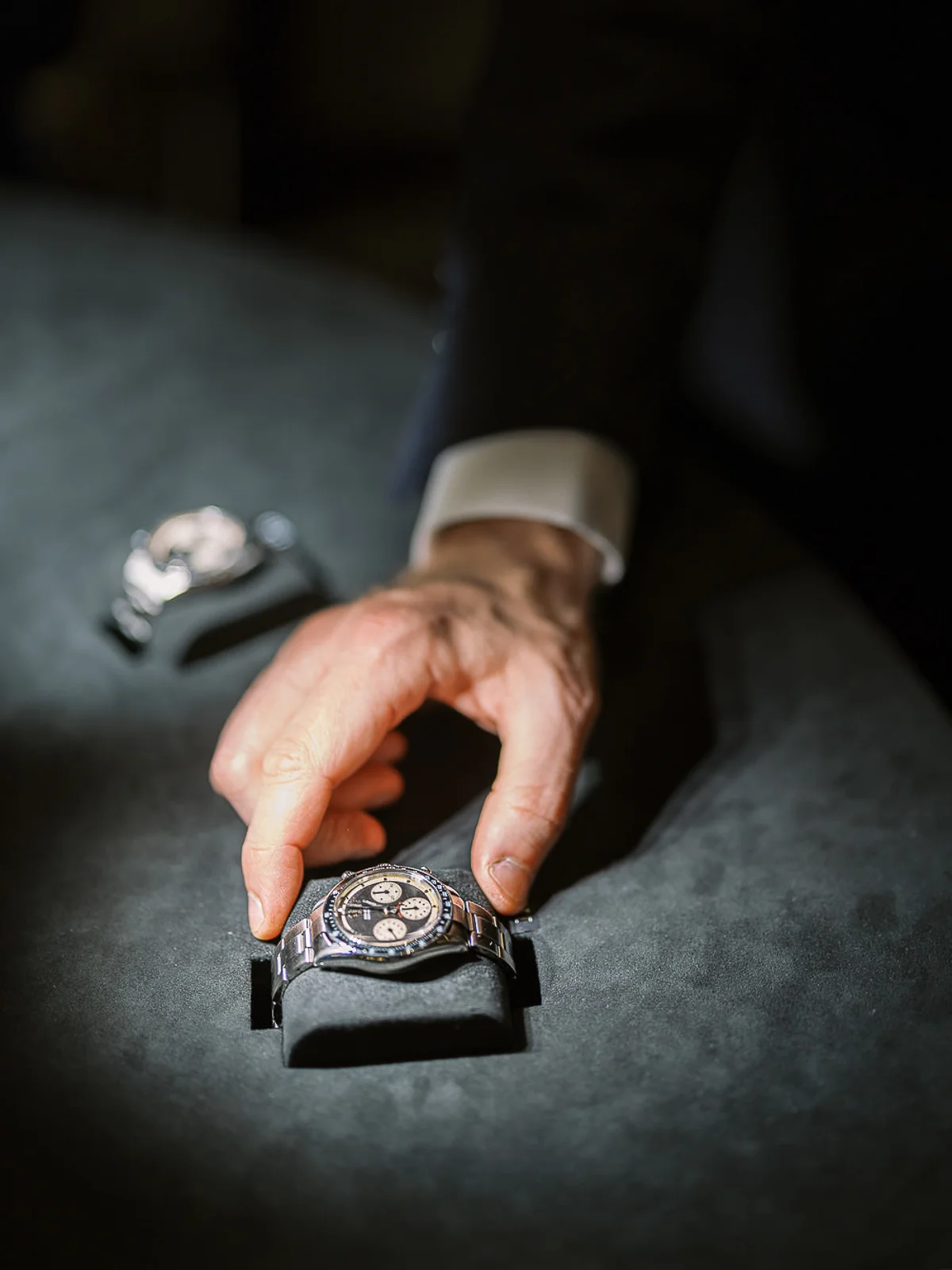 Photographe reportage Rhône Alpes : main d'homme en costume présentant une montre chronographe de luxe sur un présentoir.