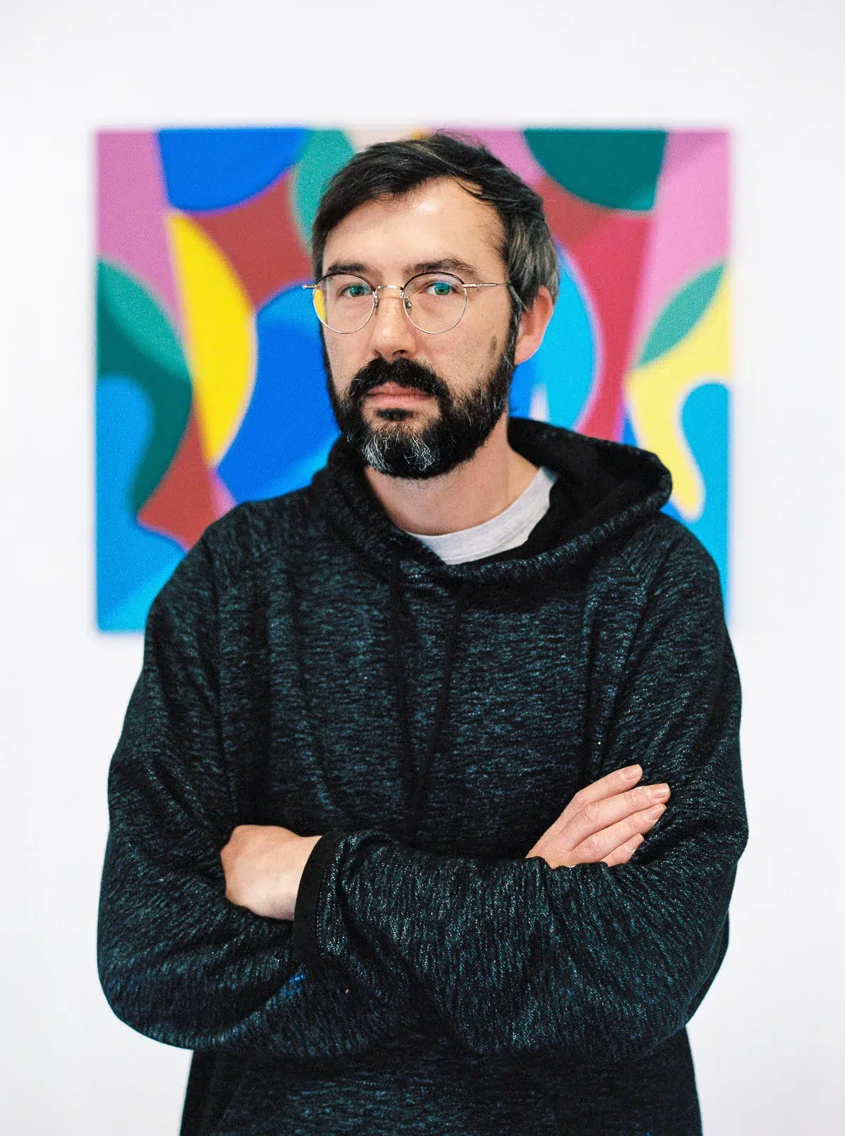 Photographe portrait Lyon : homme barbu à lunettes devant un tableau abstrait coloré.