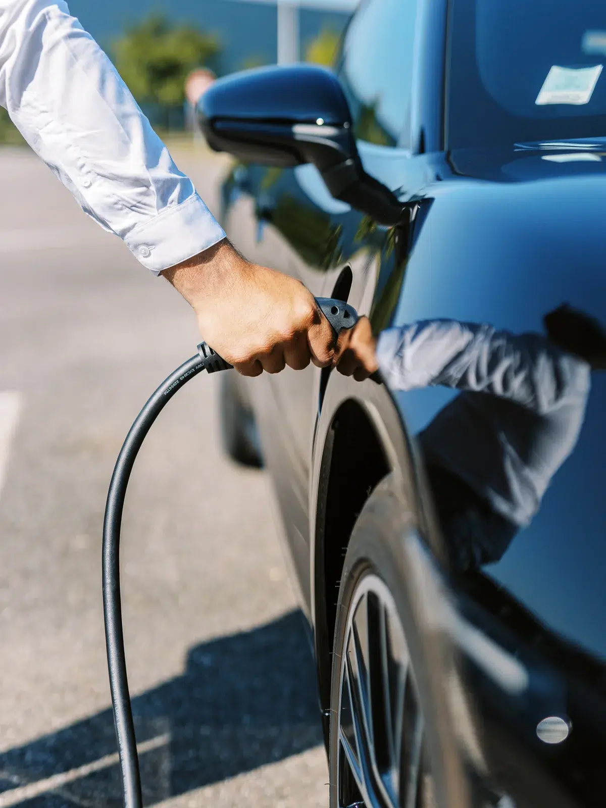 Photographe reportage Lyon : Une main branche un câble de recharge sur une voiture électrique noire.