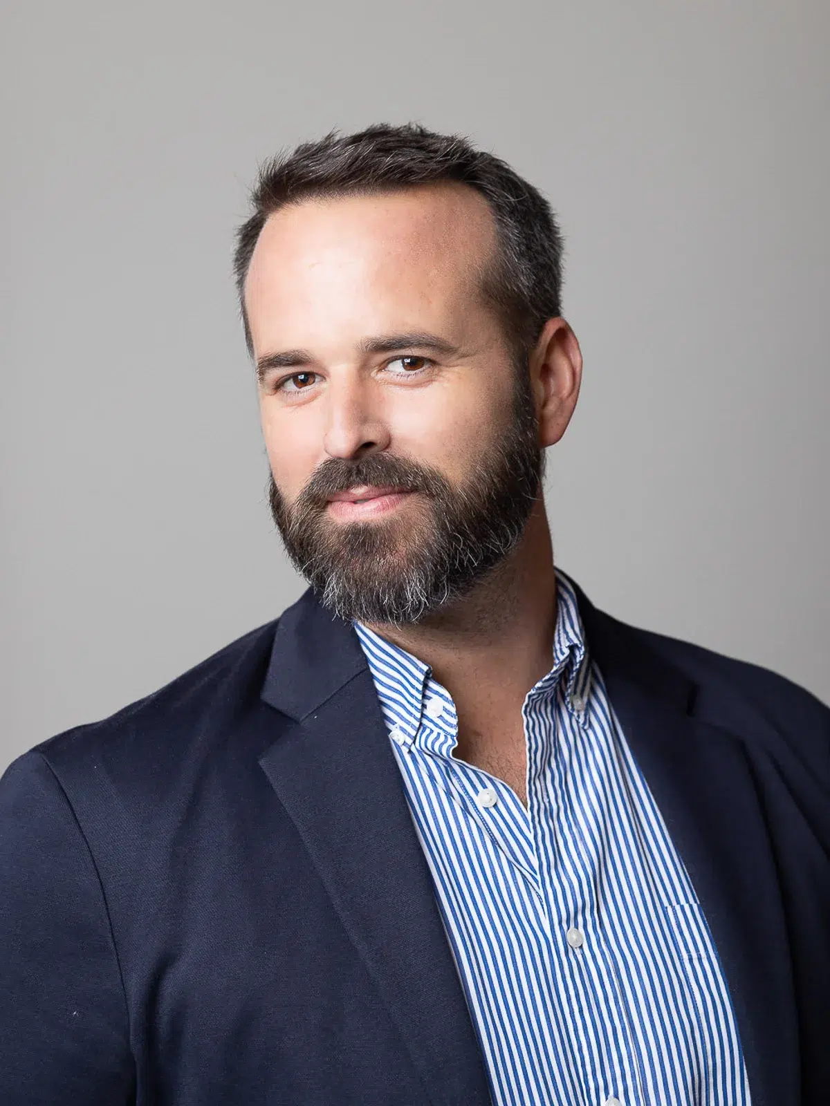 Photographe portrait Lyon : homme barbu en blazer bleu marine et chemise à rayures.