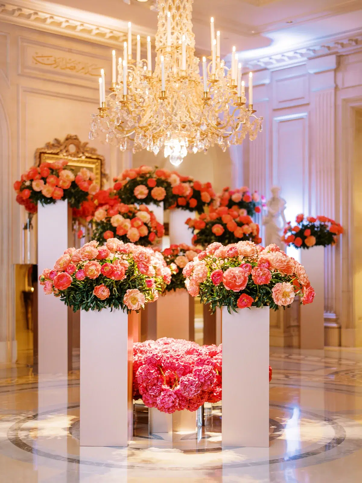 Salon d'apparat avec lustres et pivoines roses, mis en lumière par un photographe architecture Lyon.