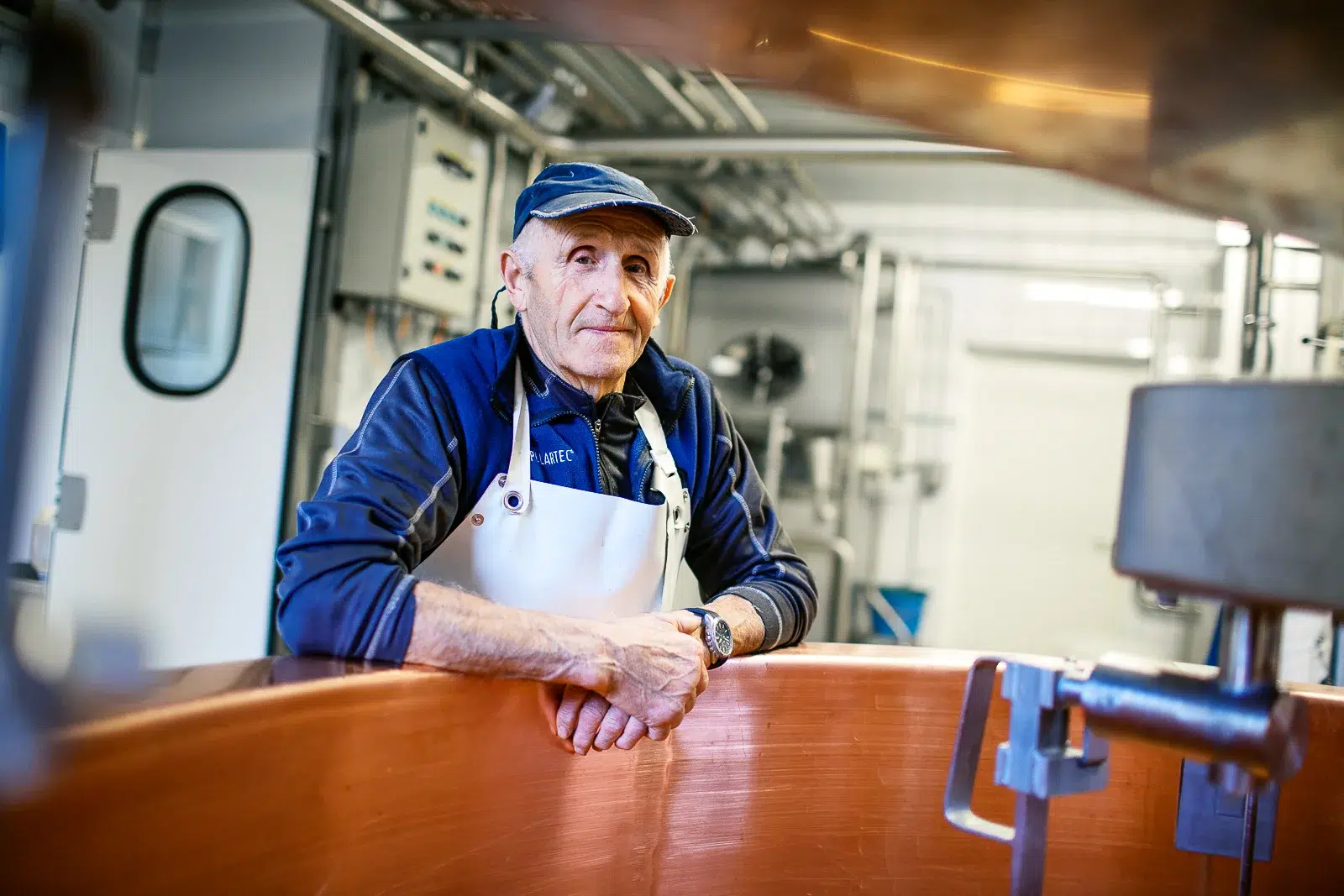 Photographe reportage Lyon : portrait d'un artisan fromager accoudé à une cuve en cuivre dans son atelier de fabrication.