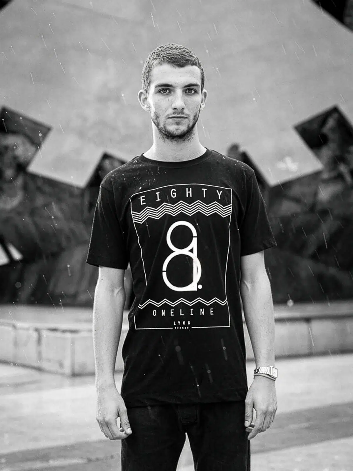 Photographe portrait Lyon : jeune homme en t-shirt "Eighty One" devant une sculpture.