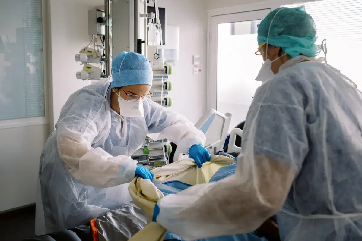 Reportage photo Lyon : Deux infirmières en tenue de protection s'occupent d'un patient alité.