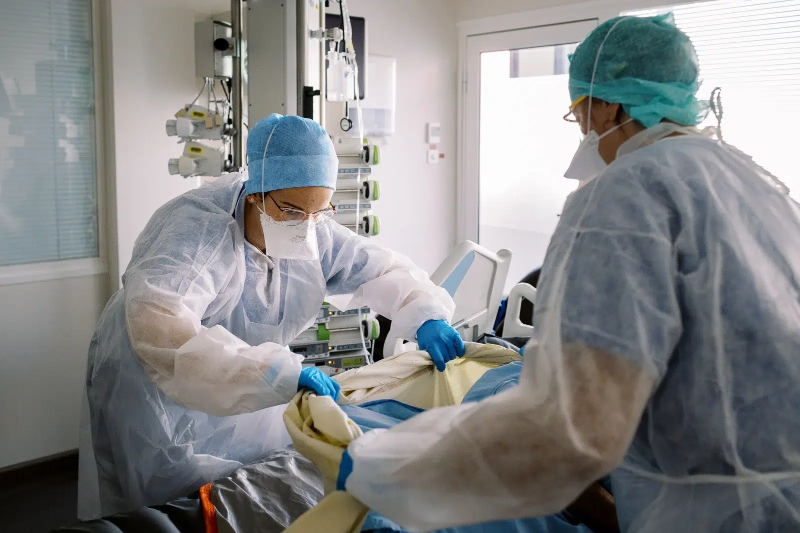 Reportage photo Lyon : Deux infirmières en tenue de protection s'occupent d'un patient alité.