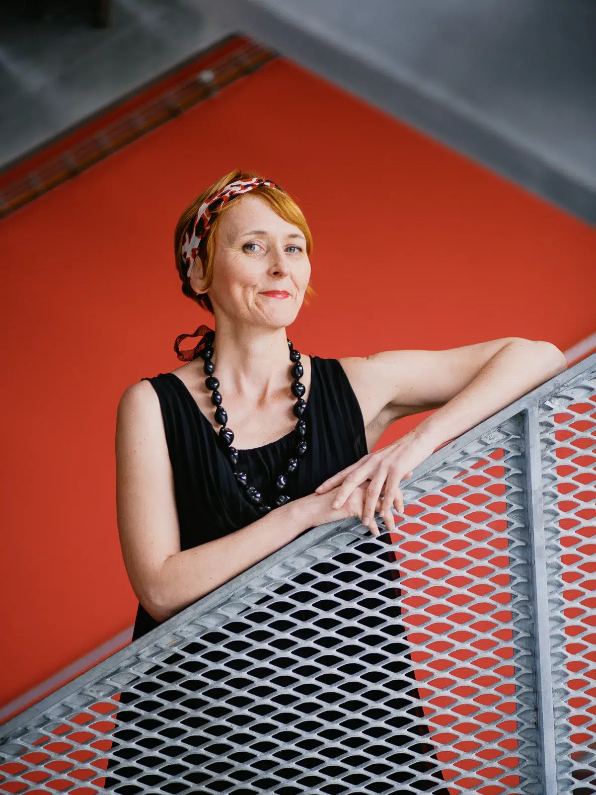 Photographe portrait Lyon : femme rousse en robe noire devant un mur rouge vif.