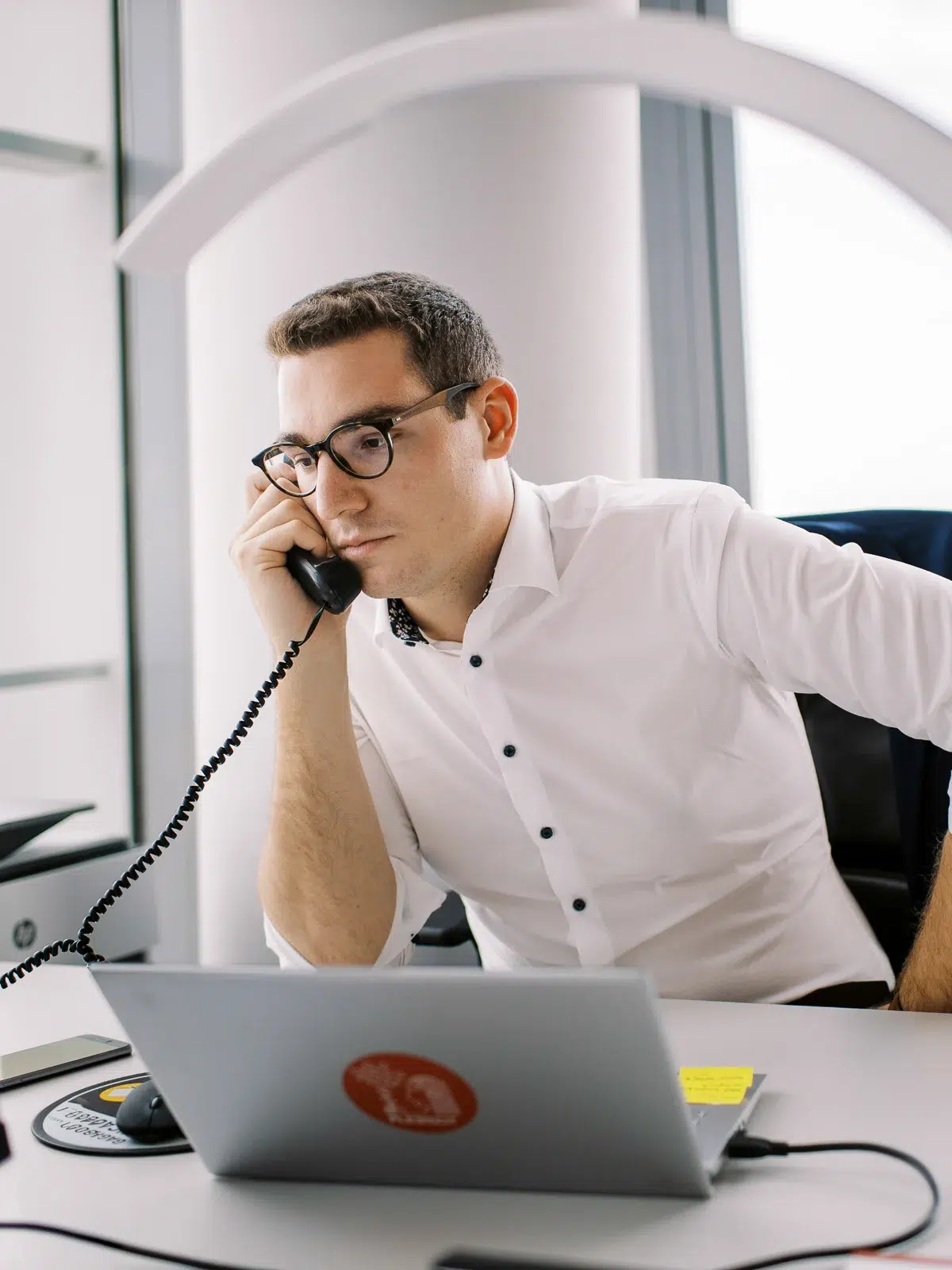Photo reportage Rhône Alpes : Un homme en chemise blanche téléphone à son bureau, l'air concentré.