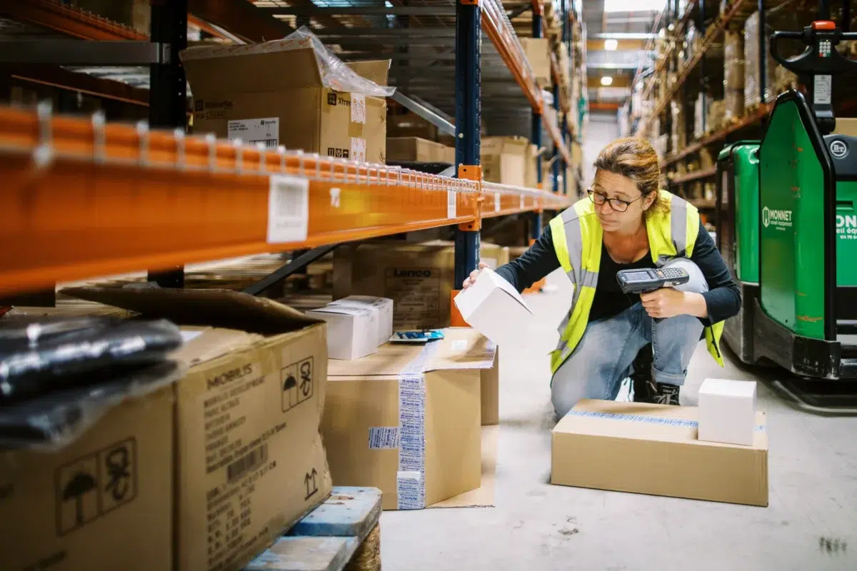 Photographe reportage Lyon : employée en gilet jaune scannant des colis avec un terminal dans les allées d'un entrepôt logistique.
