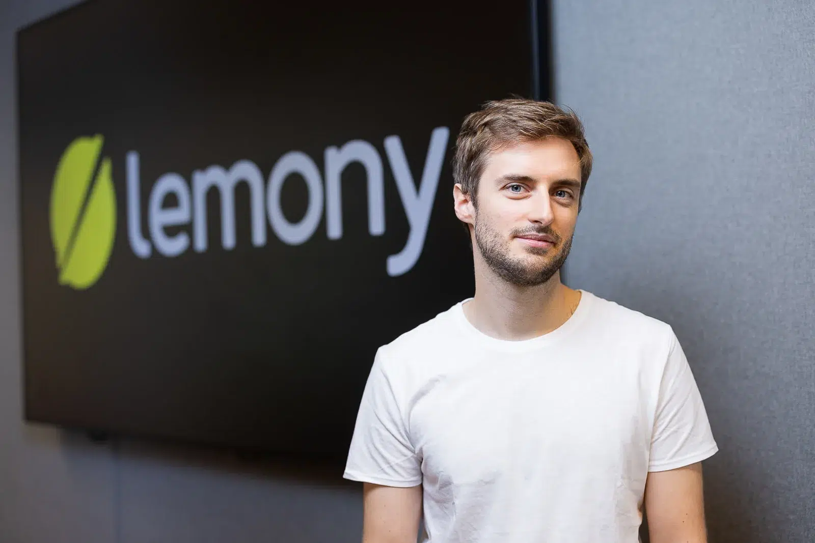 Photographe portrait Lyon : jeune entrepreneur devant le logo Lemony en bureau moderne.