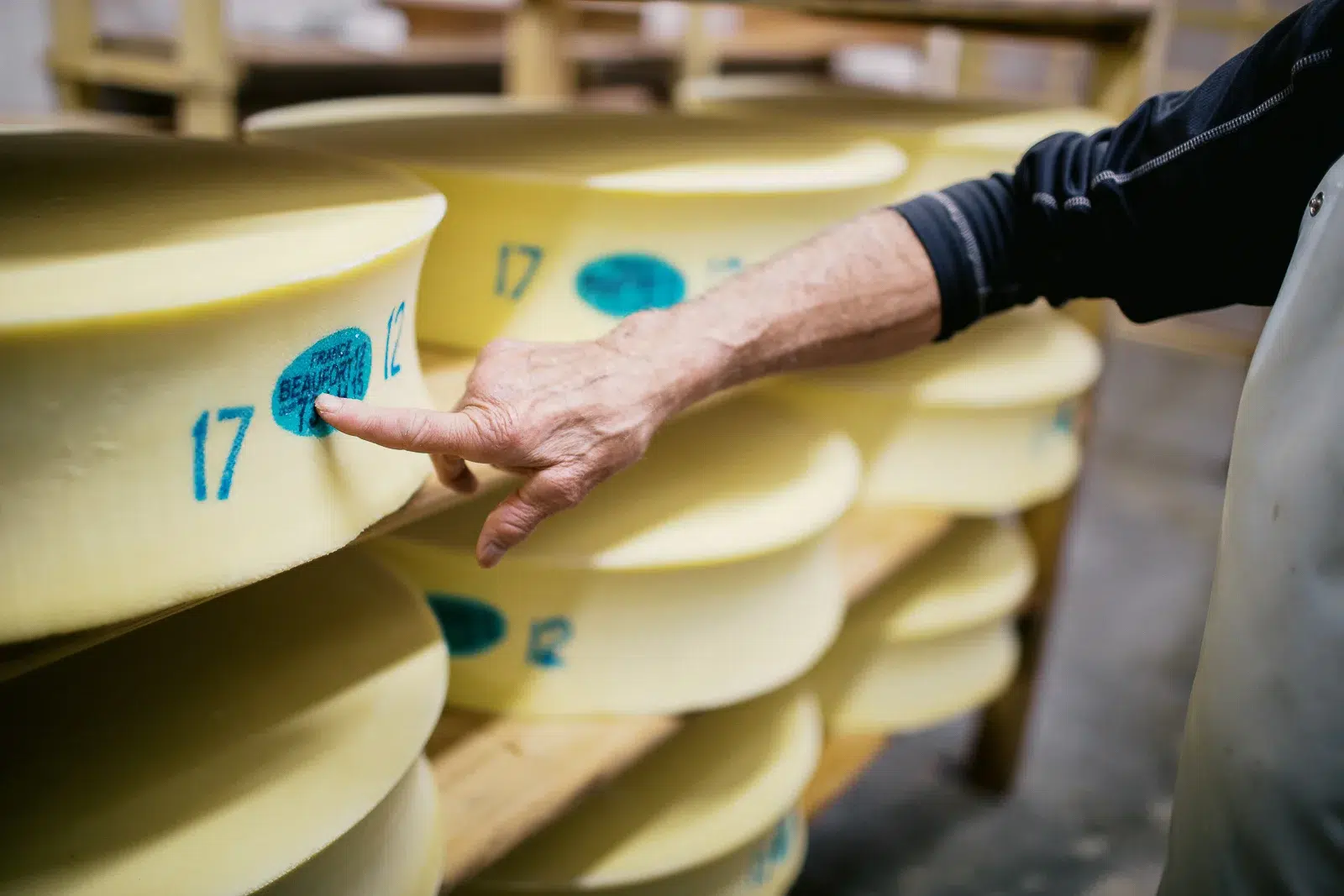 Reportage photo Lyon : Un artisan fromager montre l'étiquette d'une meule de Beaufort en cave.