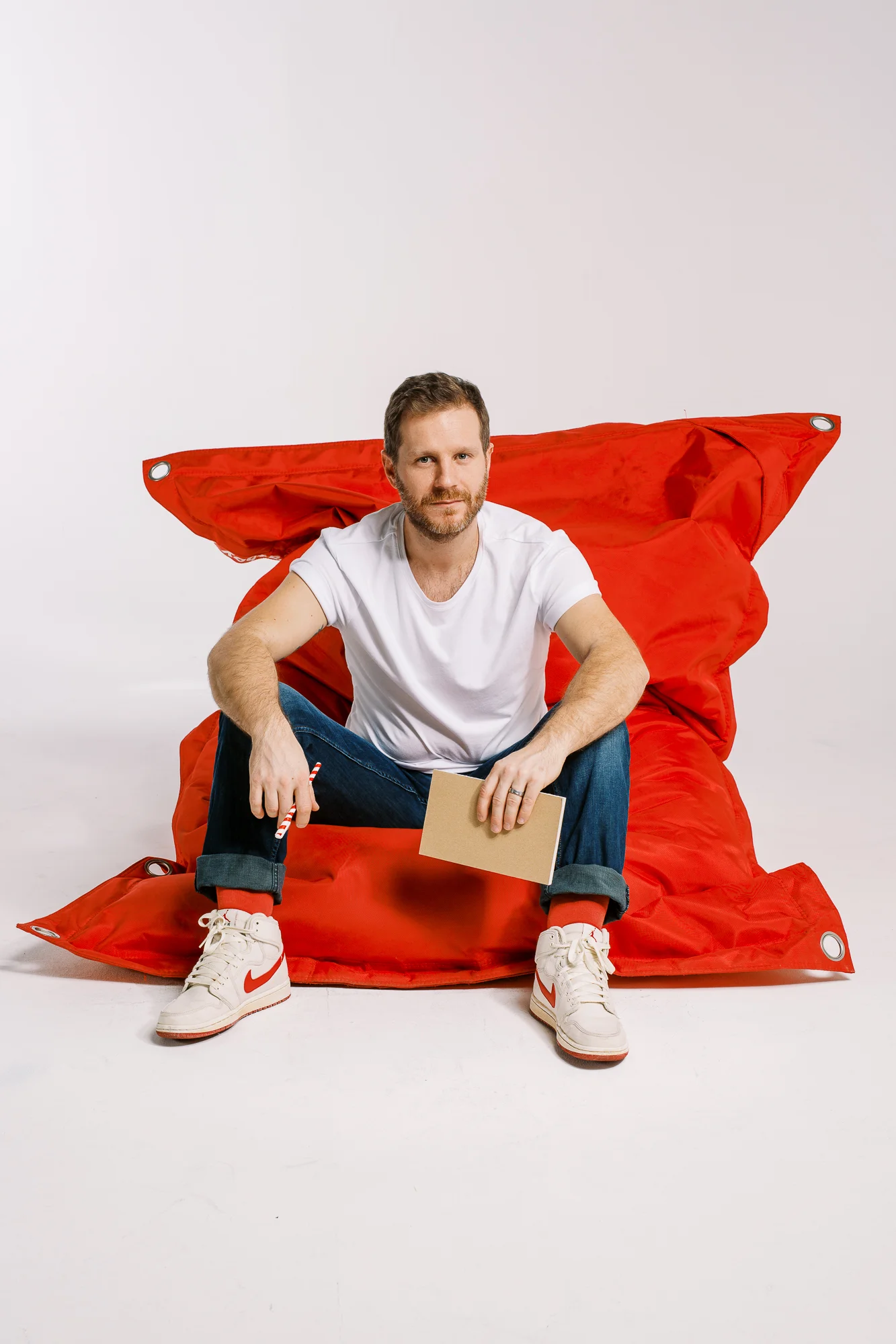 Agence de communication Hula Hoop : homme assis sur un grand pouf rouge tenant un carnet et un stylo rayé.