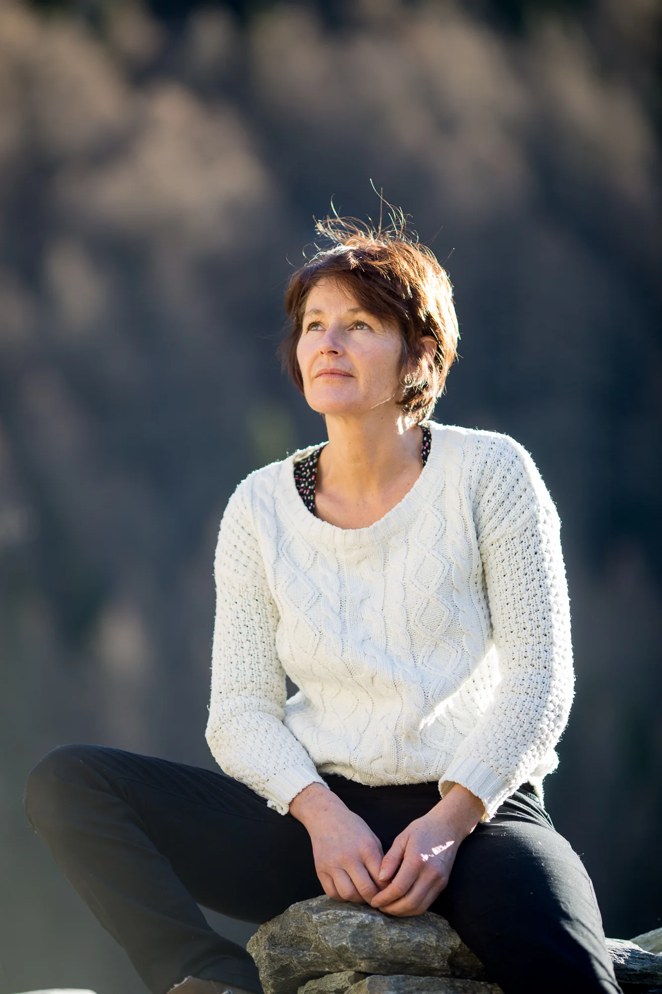 Photographe en Savoie : femme assise sur un rocher contemplant les sommets alpins.