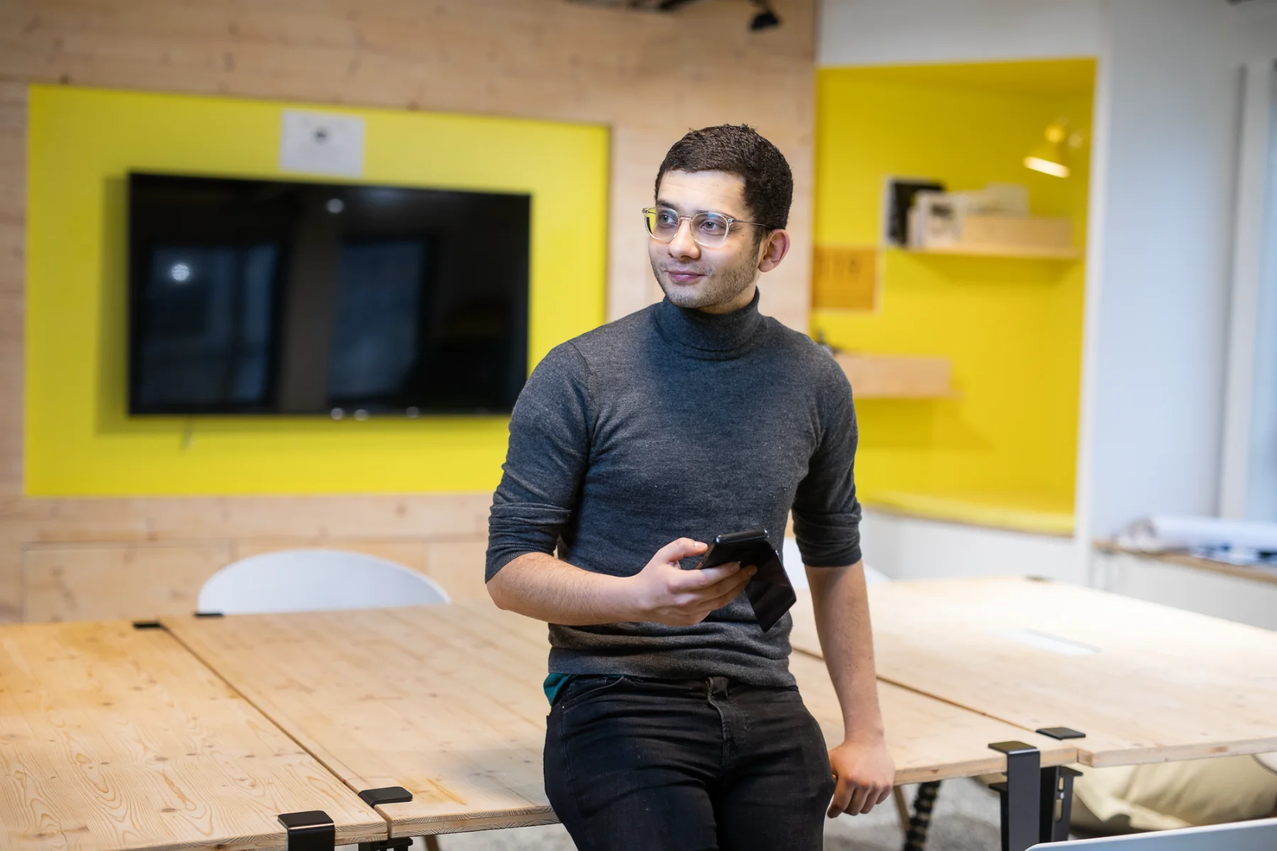 Jeune professionnel avec smartphone dans un bureau moderne, idéal pour comparer les tarifs photo corporate.